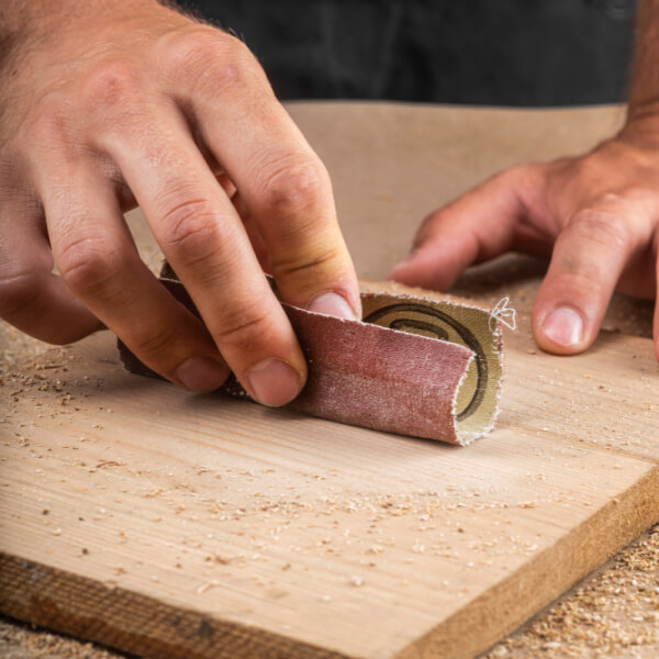 Gros plan de mains ponçant un morceau de bois plat avec du papier de verre plié.