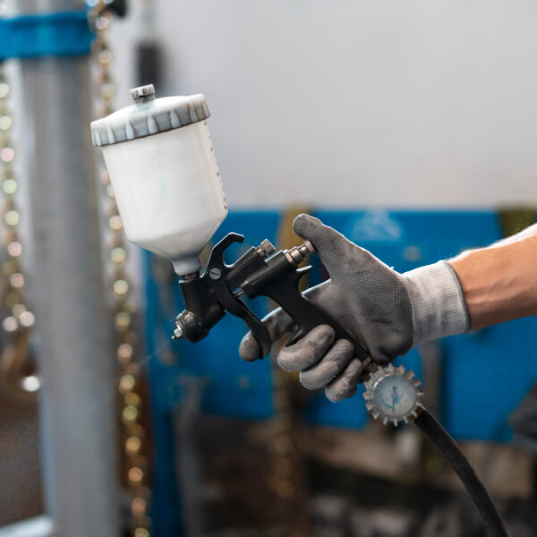 Une main gantée tenant un pistolet de peinture pneumatique dans un atelier de carrosserie.