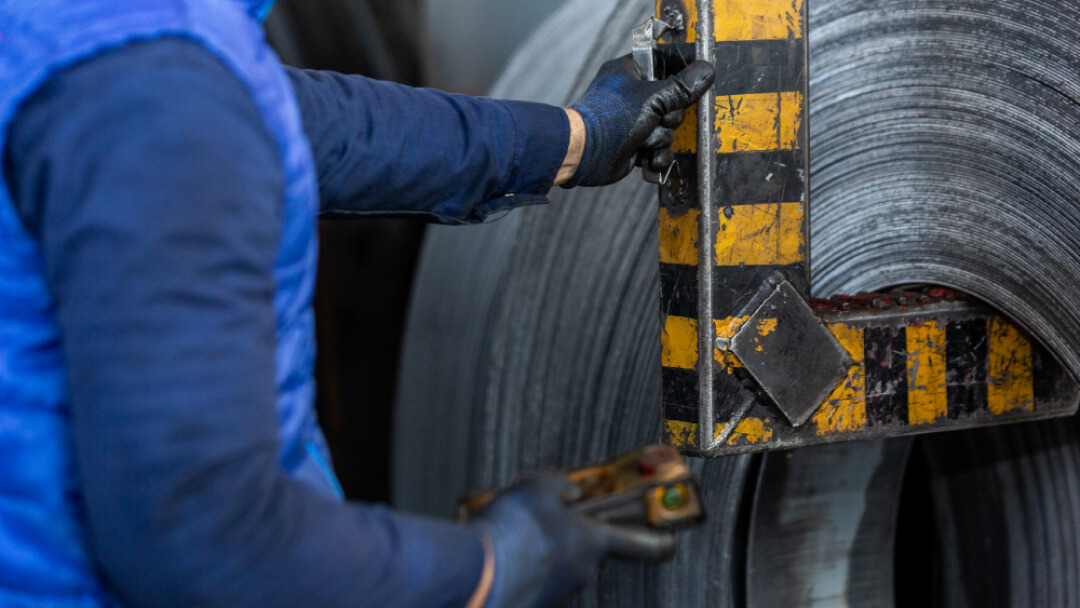 Un travailleur industriel manipulant de grandes bobines d'acier avec un équipement de levage.