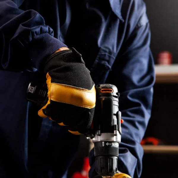 Un homme en chemise bleue et gants noirs utilise une perceuse.