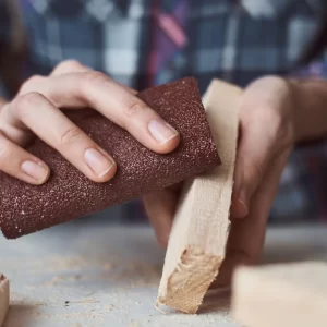 Une personne ponce du bois avec un bloc de ponçage, concentrée sur son travail.